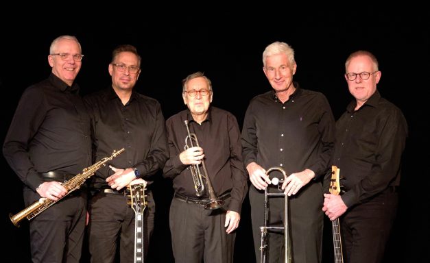 Fünf Musiker in schwarzer Kleidung mit verschiedenen Instrumenten.